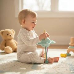 Baby spielt mit farbenfrohem Holzspielzeug auf Teppich, neben Plüschbär – nachhaltiges Spielzeug für Kleinkinder